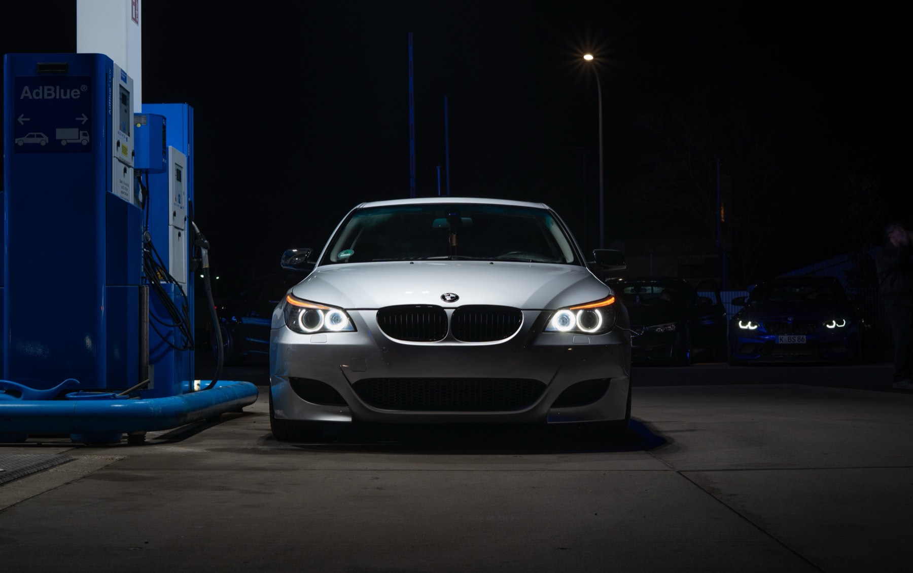 Silberner BMW E60 nachts an einer Tankstelle
