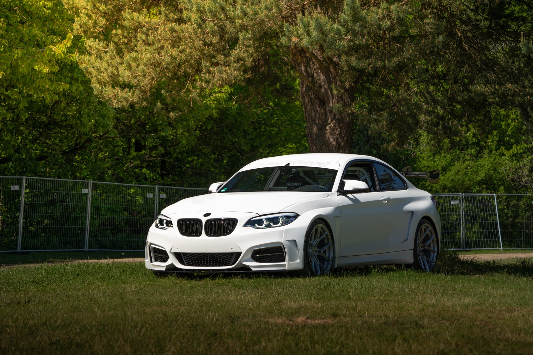 Weißer BMW M240i Manhart auf einer Wiese vor Bäumen