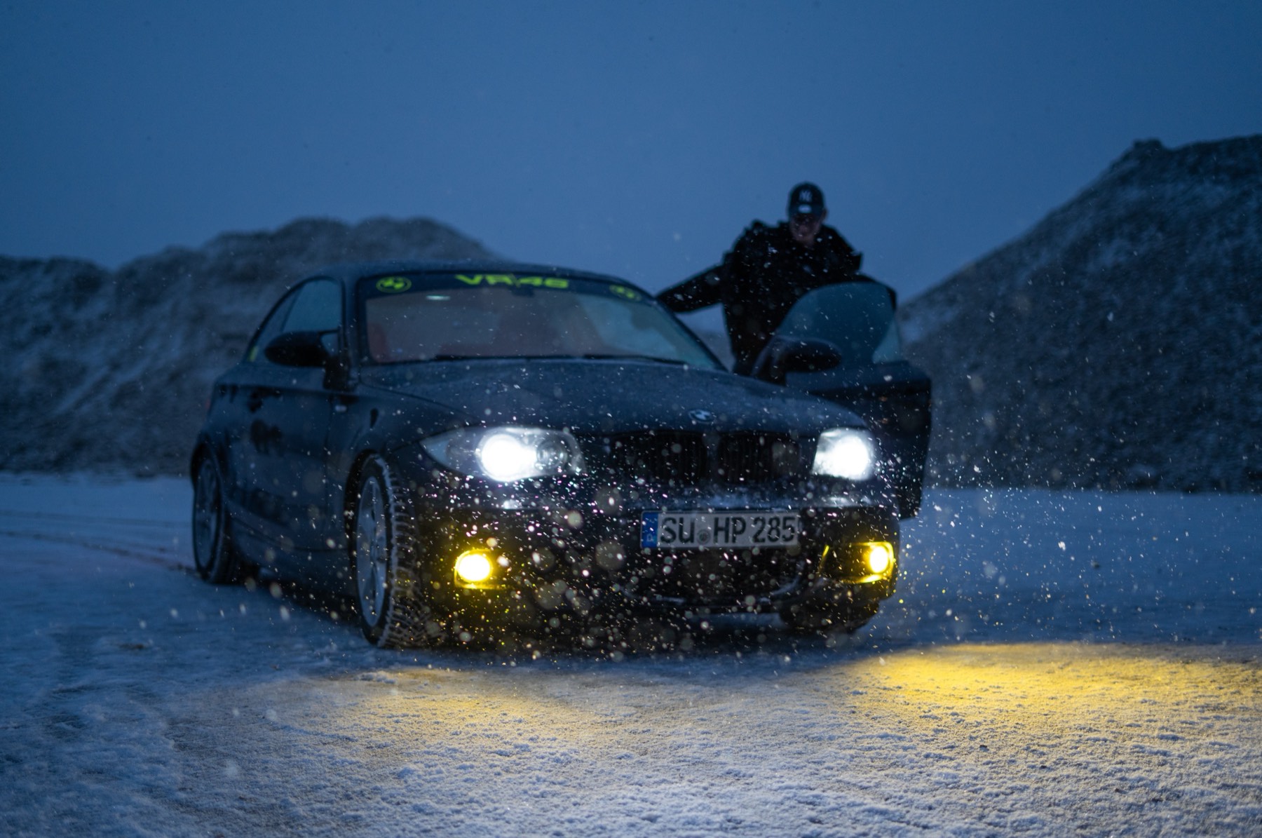 Dunkler BMW bei Schneefall, eine Person steht in der geöffneten Fahrertür